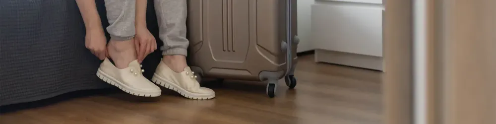 Close up of person putting on shoes next to rolling luggage